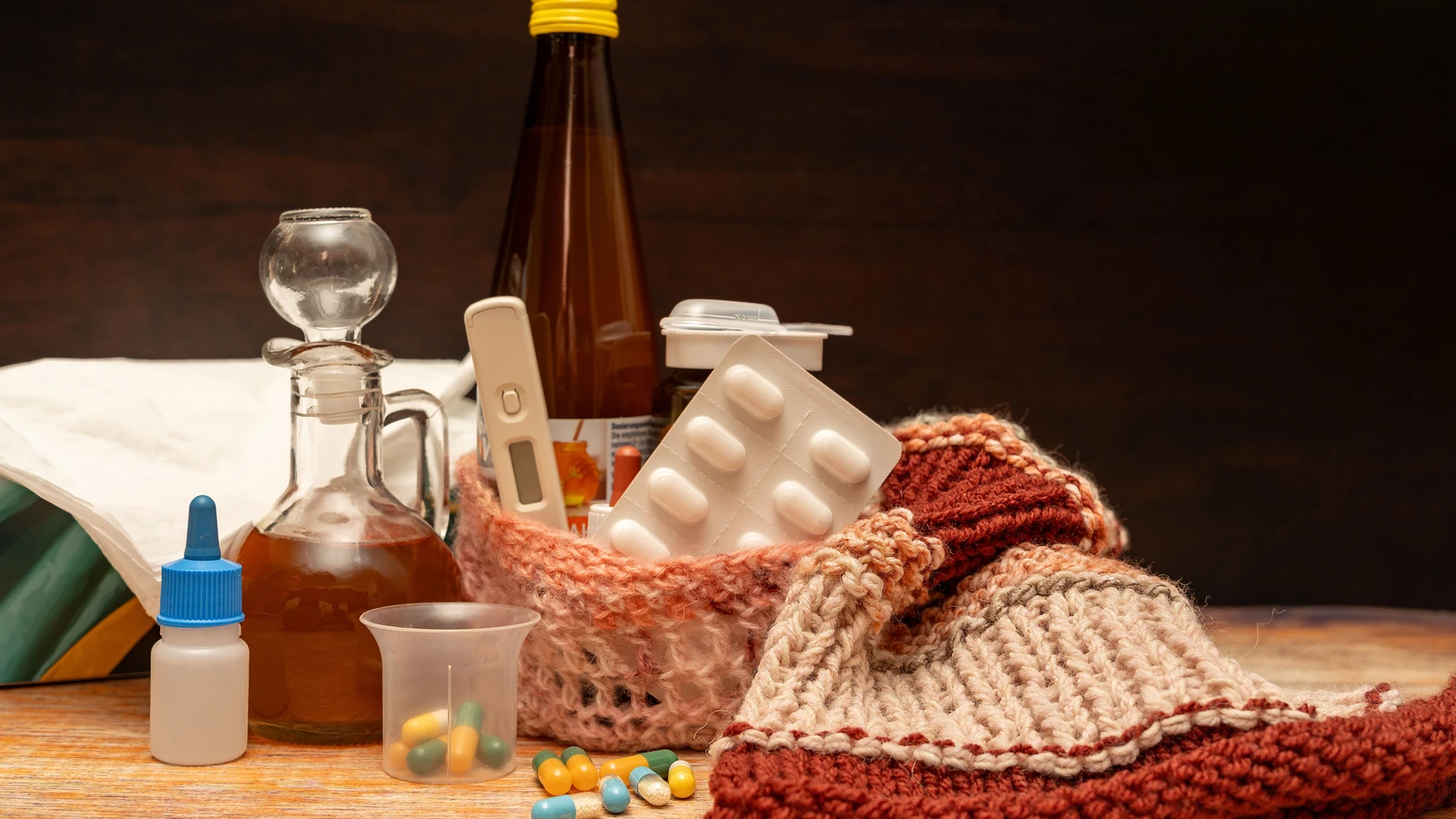 Una calda collezione di medicinali e articoli per alleviare il raffreddore e l'influenza, disposti su una superficie di legno.