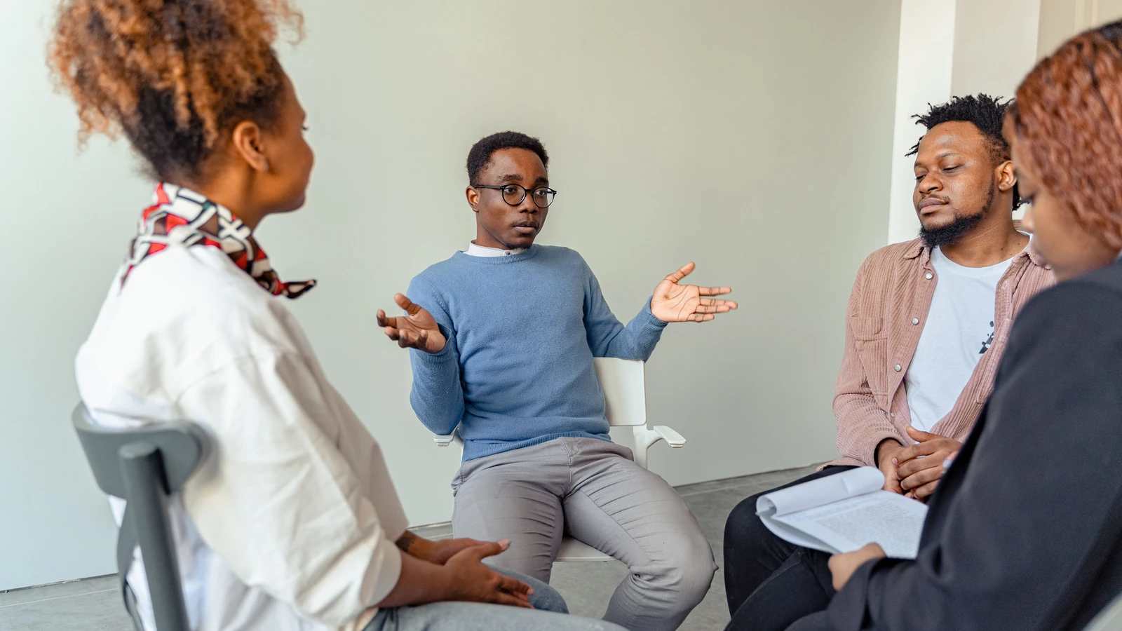 Sessione di terapia di gruppo diversificata con giovani adulti e un professionista della salute mentale al coperto.