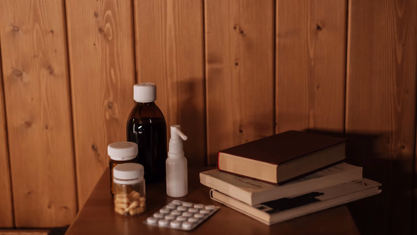 Una scena interna accogliente con medicinali e libri su un comodino di legno, che offre un'atmosfera calda e rustica. — Ron Lach – Pexels