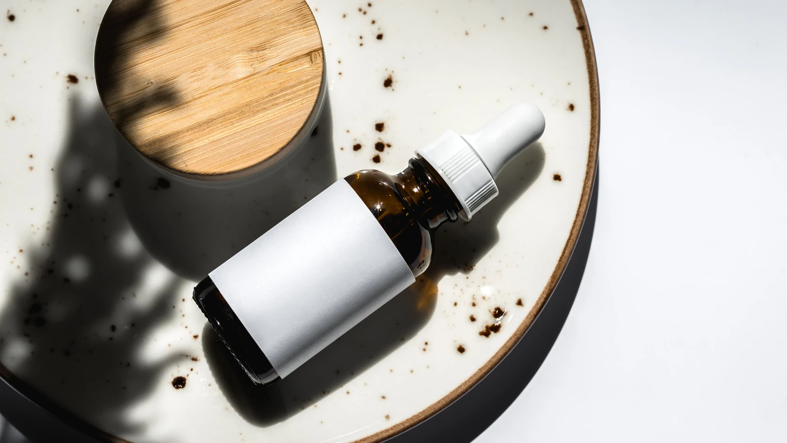Composizione elegante di una bottiglia contagocce essenziale per la cura della pelle su un piatto in ceramica. Perfetto per branding di prodotto e blog di bellezza.