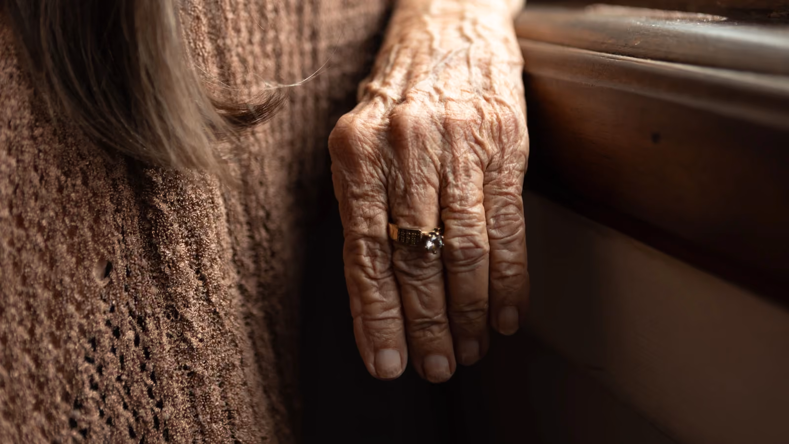 Primo piano di una mano anziana con anello che evidenzia rughe e texture su sfondo di tessuto marrone — Elizabeth Ferreira – Pexels