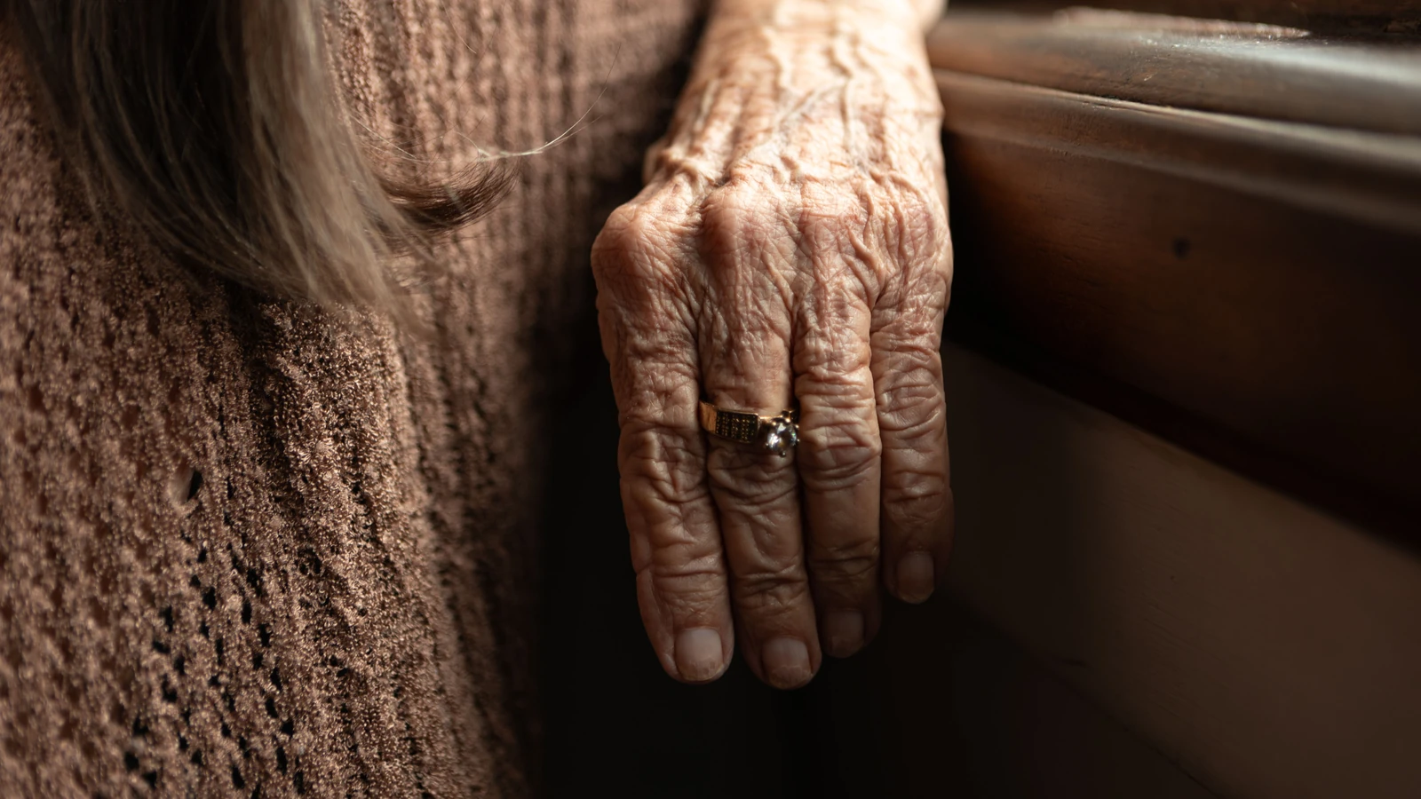 Primo piano di una mano anziana con anello che evidenzia rughe e texture su sfondo di tessuto marrone — Elizabeth Ferreira – Pexels