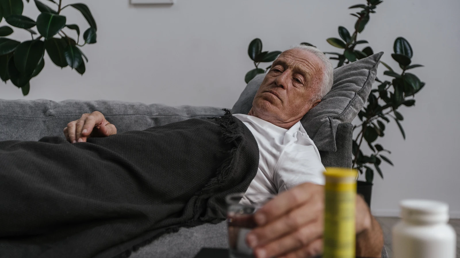 Uomo anziano sdraiato sul divano con farmaci, si sente male e riposa in casa.