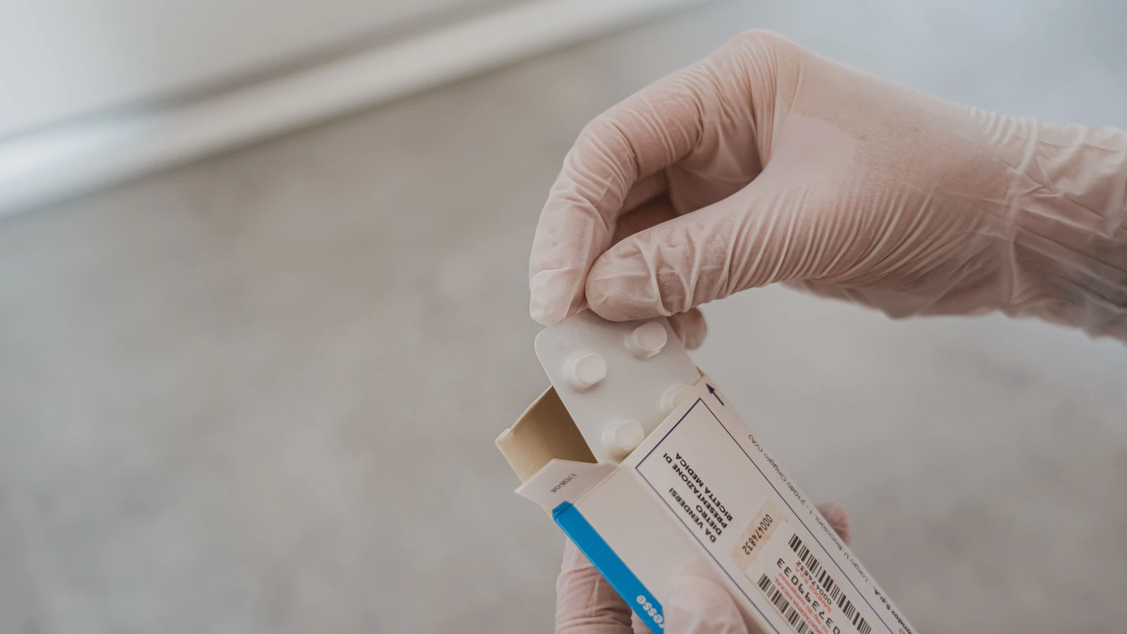 Primo piano di mani in guanti che maneggiano una confezione blister di farmaci, garantendo sicurezza e igiene nella sanità.