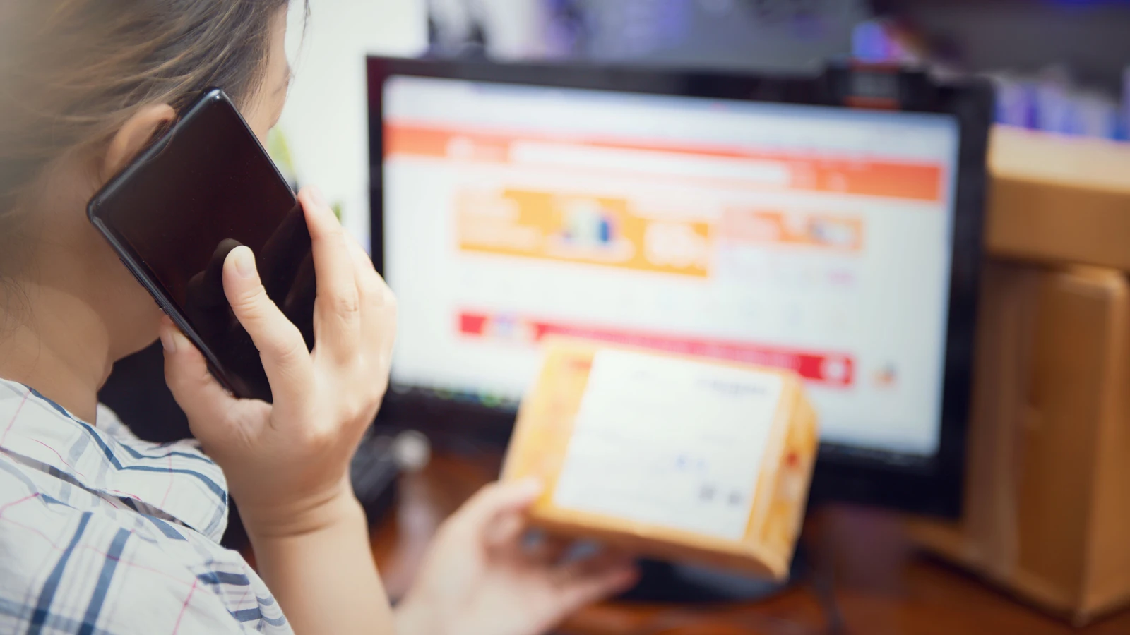 Una donna svolge più attività contemporaneamente utilizzando il telefono e controllando il pacco di un acquisto online a casa.