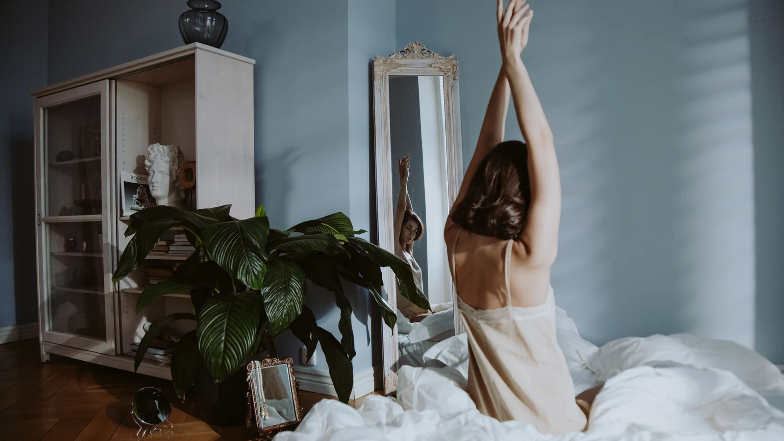 Una donna in pigiama si allunga in un ambiente tranquillo della camera da letto, riflettendosi in uno specchio.