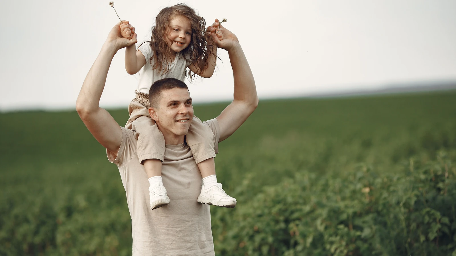 Padre felice che porta la figlia sulle spalle in un campo, godendo della natura e del legame familiare.