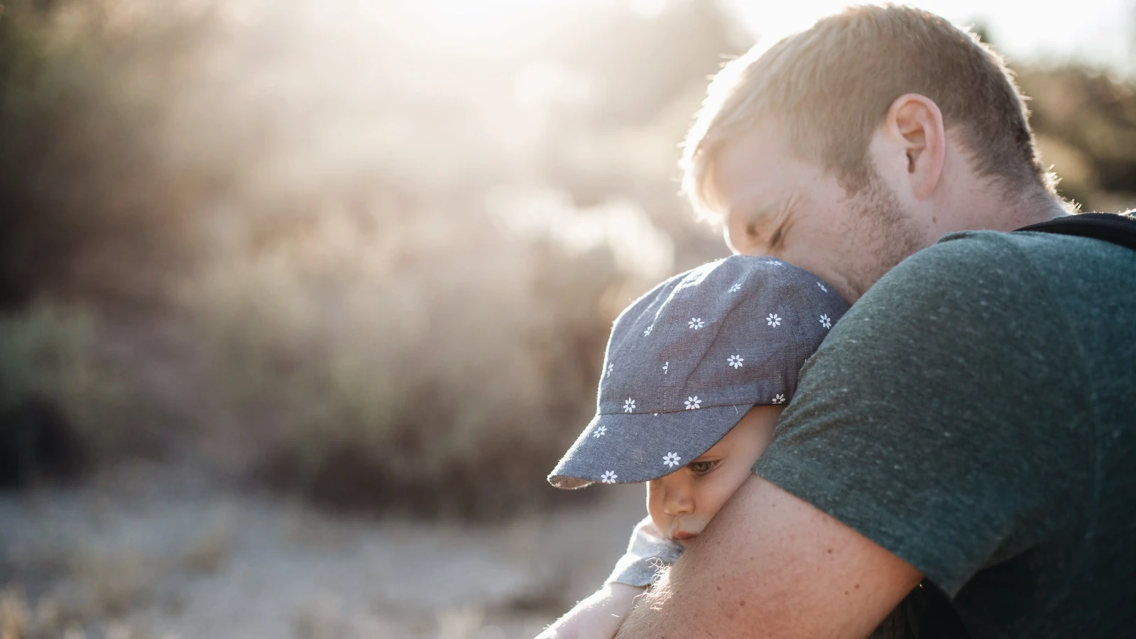 Un padre abbraccia amorevolmente il suo bambino all'aperto in una giornata di sole. Perfetto per temi della Festa del Papà.