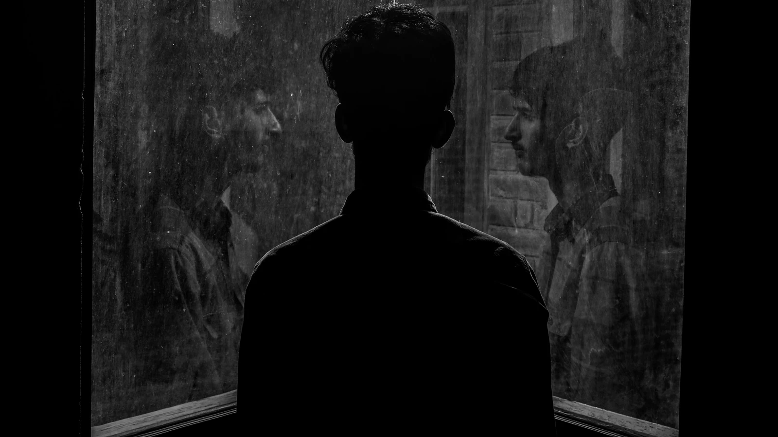Una scena contemplativa di un uomo che guarda attraverso una finestra con il suo riflesso catturato in bianco e nero.