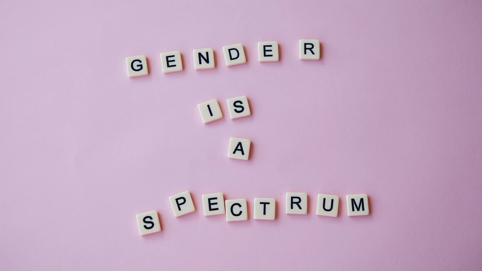 Lettere di scrabble che formano la frase 'Genere è uno Spettro' su uno sfondo rosa, simboleggiando l'inclusività LGBTQ+. — Laker – Pexels
