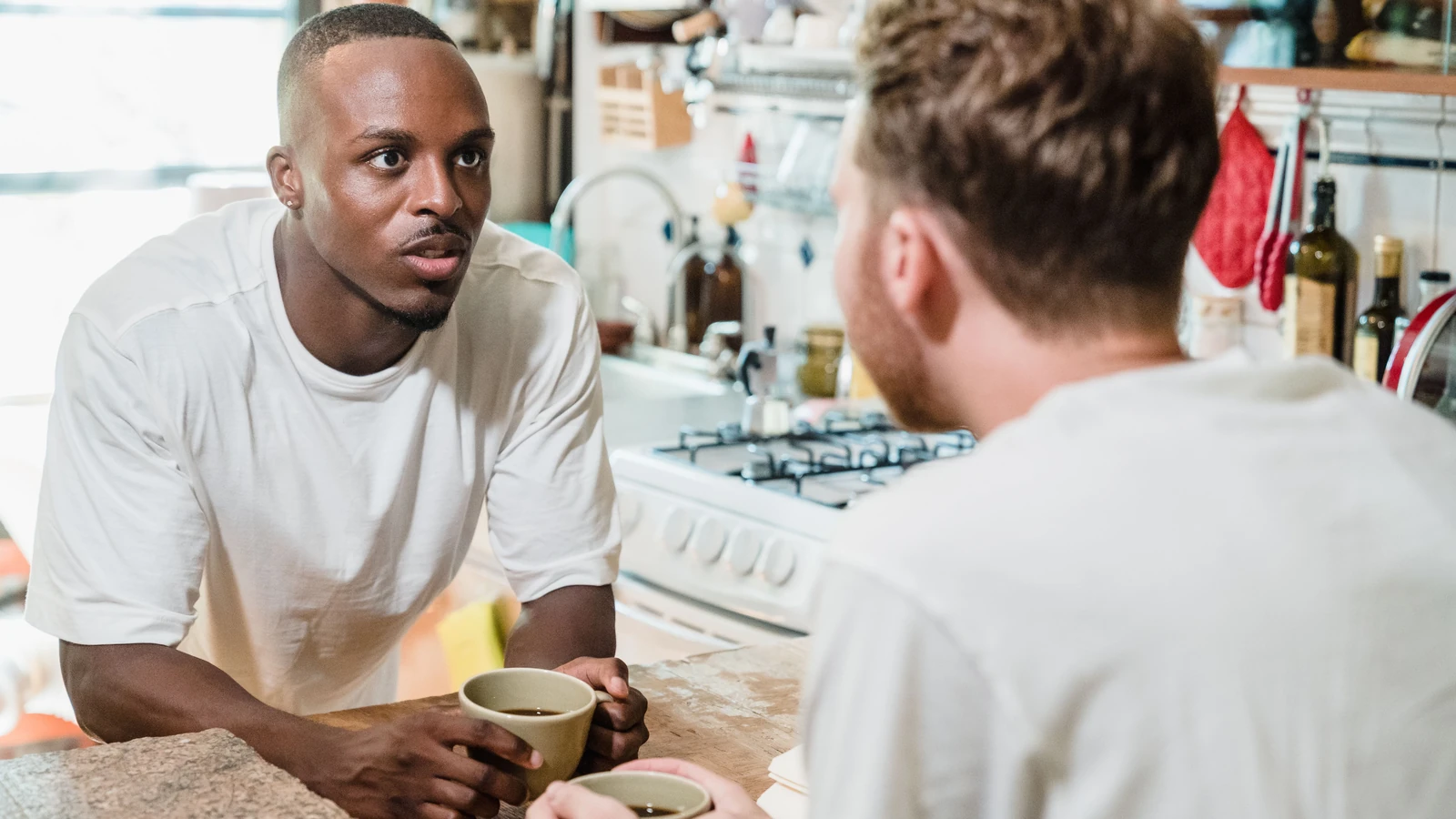 Due uomini godono di una conversazione rilassata con caffè in un ambiente cucina moderno e accogliente.