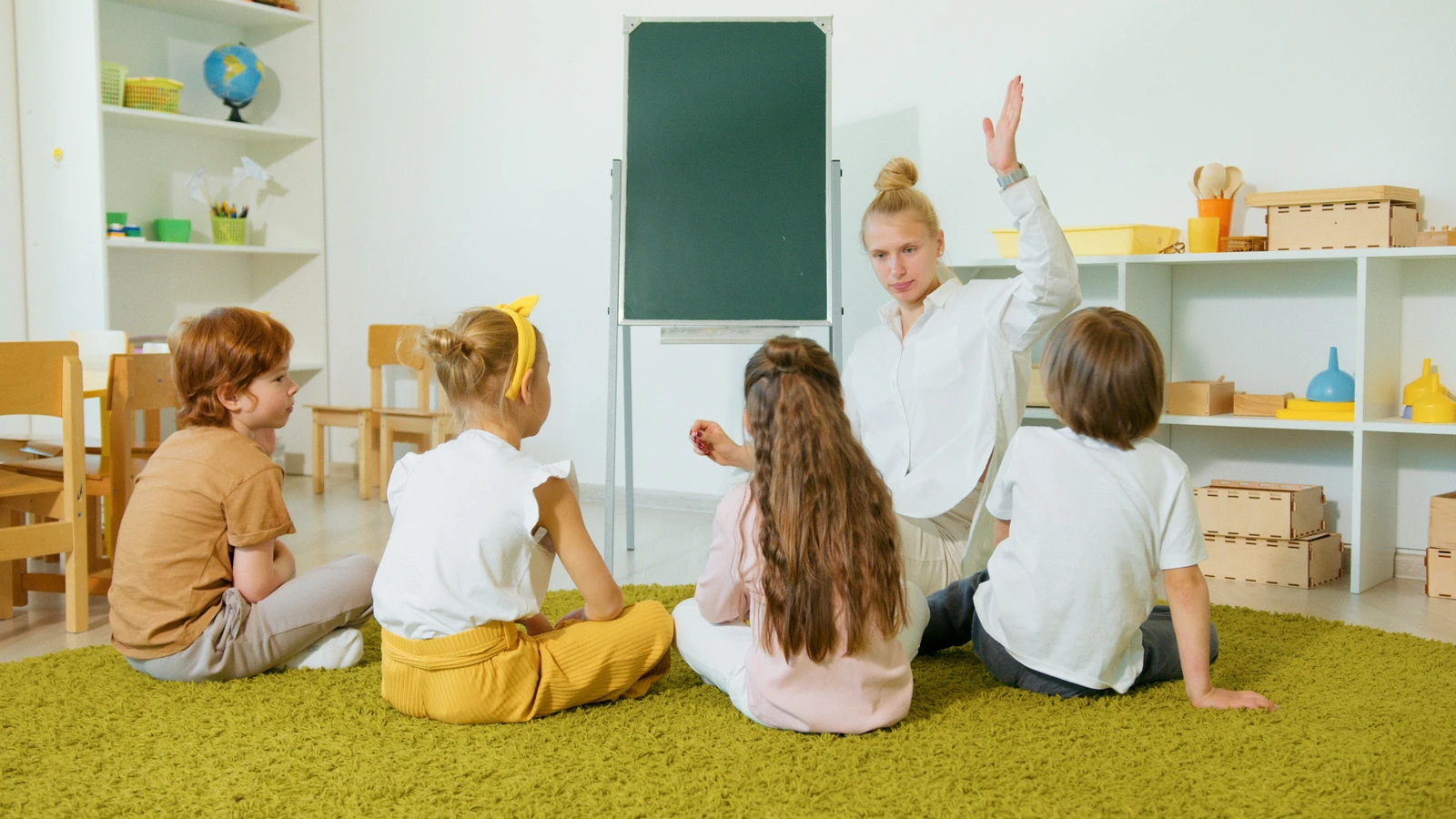 Insegnante della scuola materna che interagisce con i bambini in classe, creando un ambiente educativo e coinvolgente.