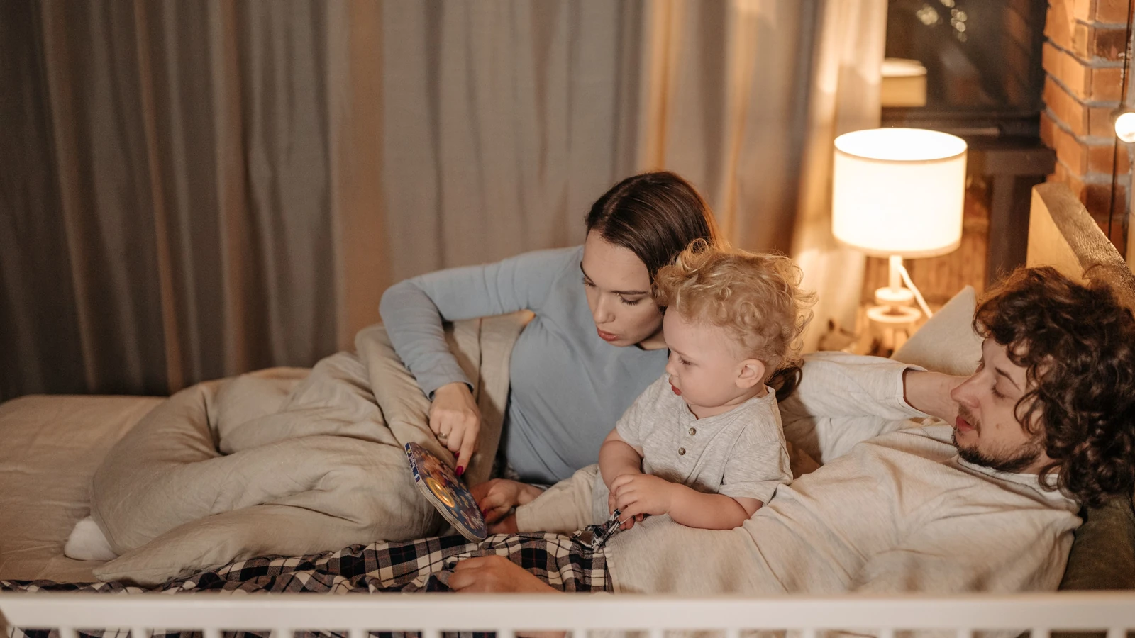 Padre e madre che leggono al loro bambino a letto durante la notte per una calda storia della buonanotte.