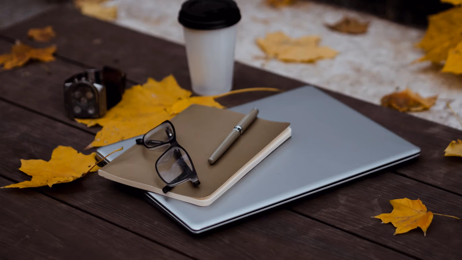 Allestimento di un'area di lavoro all'aperto in autunno con laptop, quaderno, penna e caffè su un tavolo di legno circondato da foglie cadute. — Polina ⠀ – Pexels
