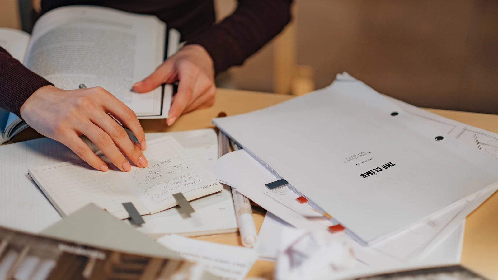Primo piano delle mani di una donna che scrive note in un quaderno per un progetto di ricerca al chiuso.