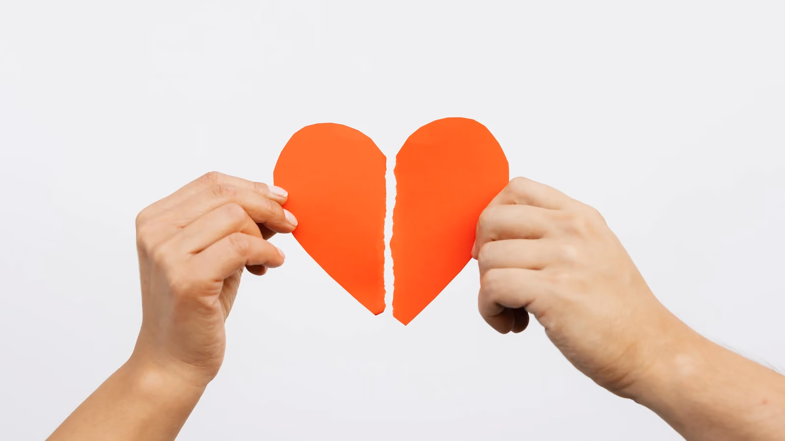 Una vista ravvicinata di mani che tengono un cuore di carta rossa strappato, simbolizzando il dolore amoroso o problemi relazionali. — https://kaboompics.com/ – Pexels