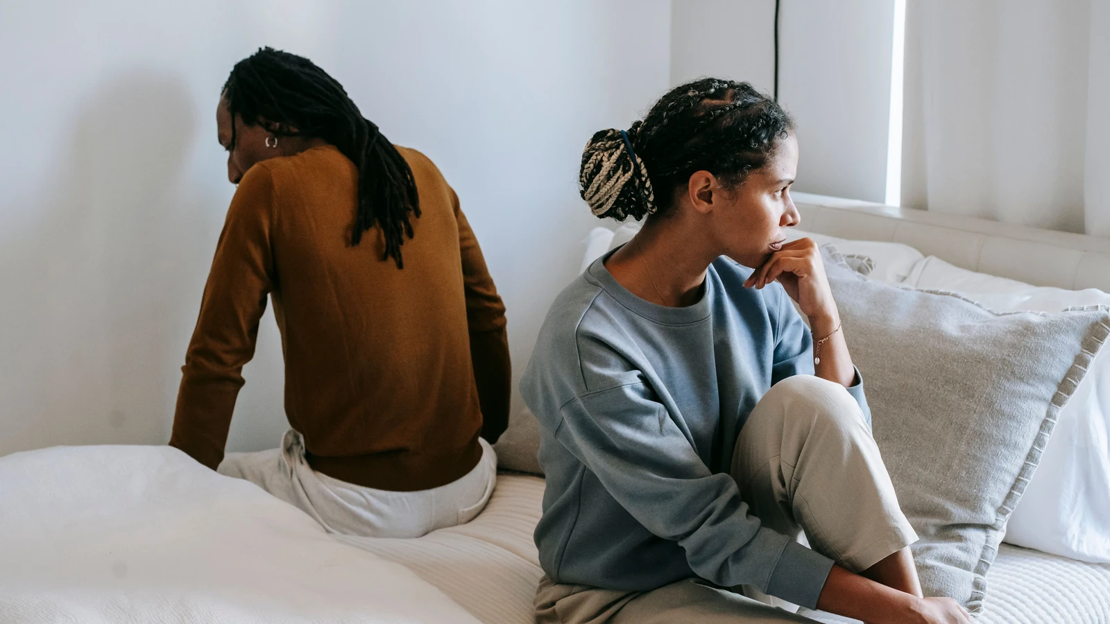 Una coppia seduta su un letto che guarda in direzioni opposte, riflettendo la tensione nella relazione.