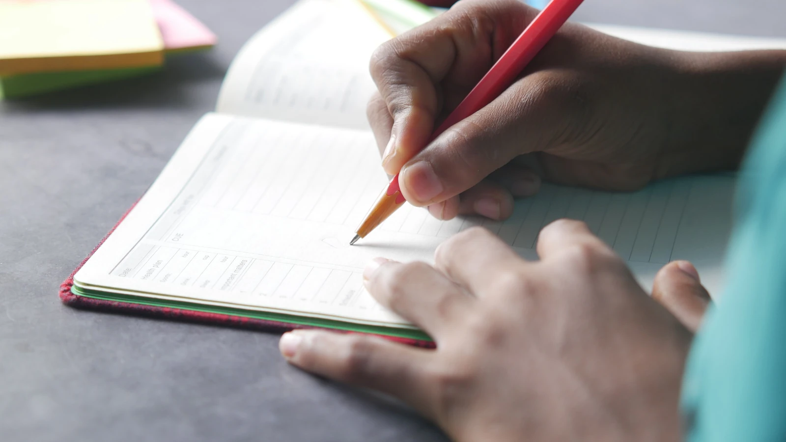 Primo piano di una mano che scrive su un quaderno con una matita in interni.