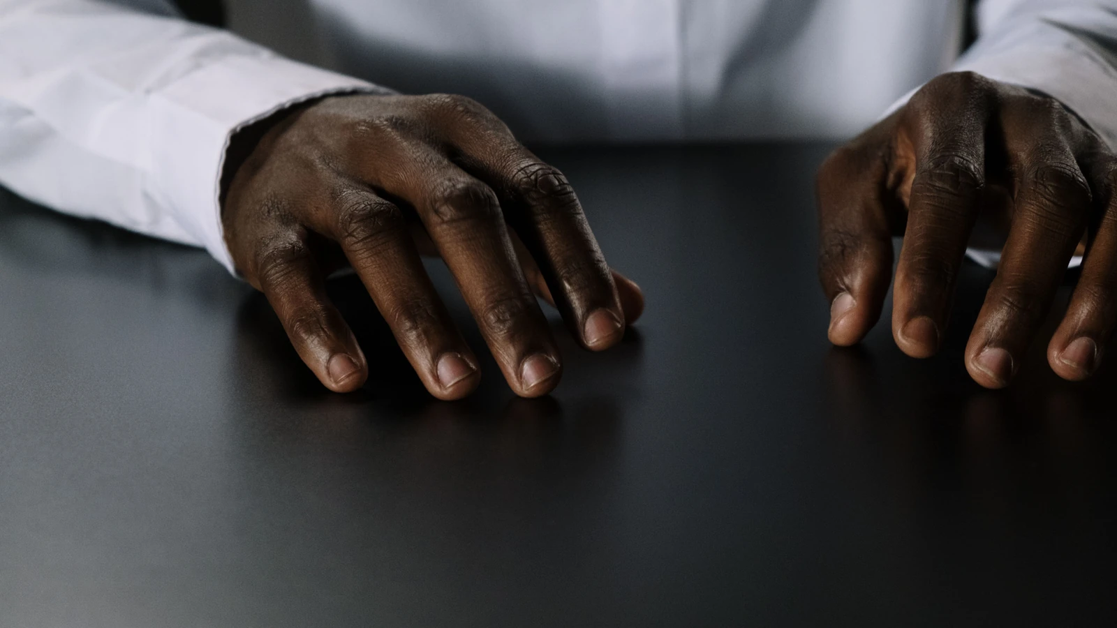 Primo piano di mani afroamericane poggiate su un tavolo, che trasmettono concentrazione e contemplazione.