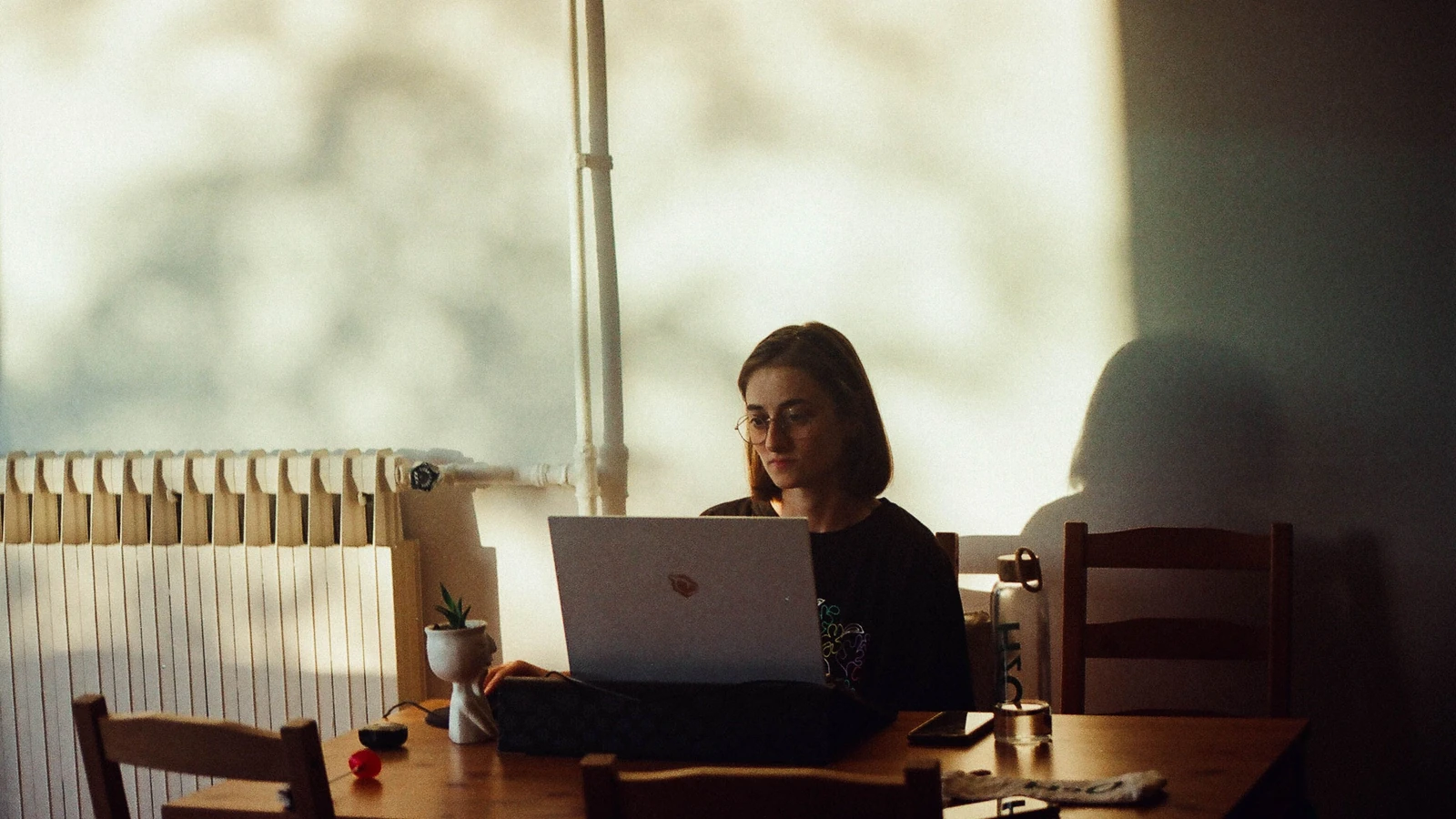 Una donna si concentra sul suo laptop in una sala da pranzo illuminata caldamente, creando un ambiente di lavoro tranquillo. — Burakcan Bakırcı – Pexels