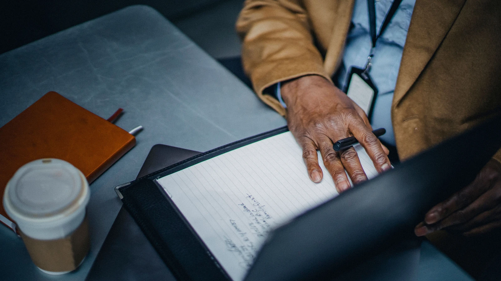Uno spazio di lavoro professionale con un quaderno, una tazza di caffè e un uomo che scrive. — Ono  Kosuki – Pexels