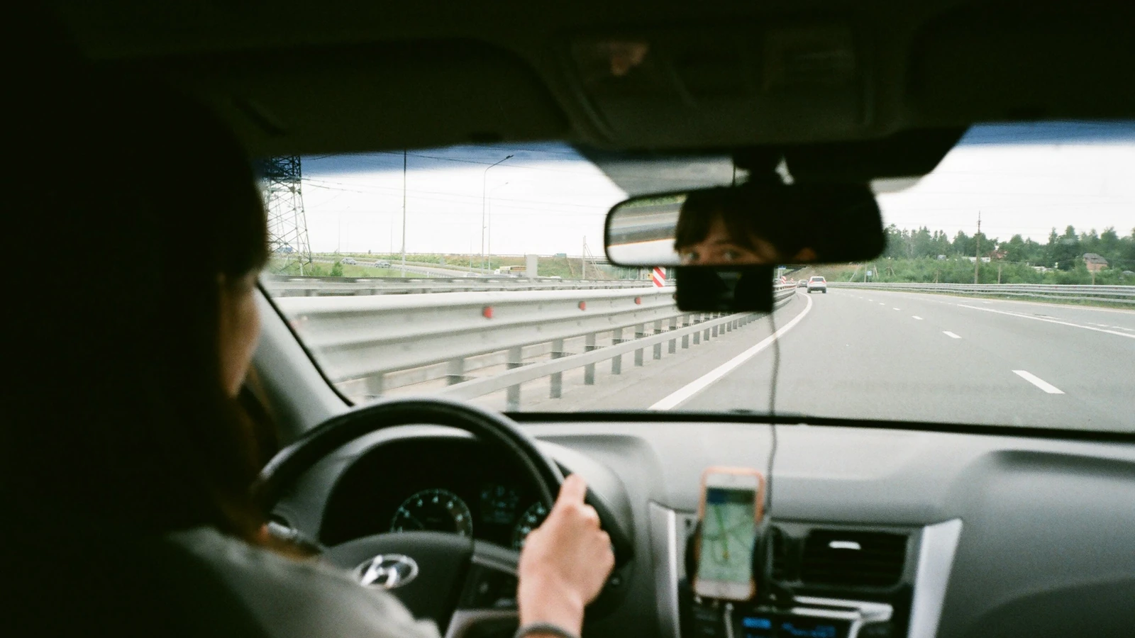 Una donna alla guida di un'auto in autostrada, utilizzando la navigazione GPS sul suo smartphone.