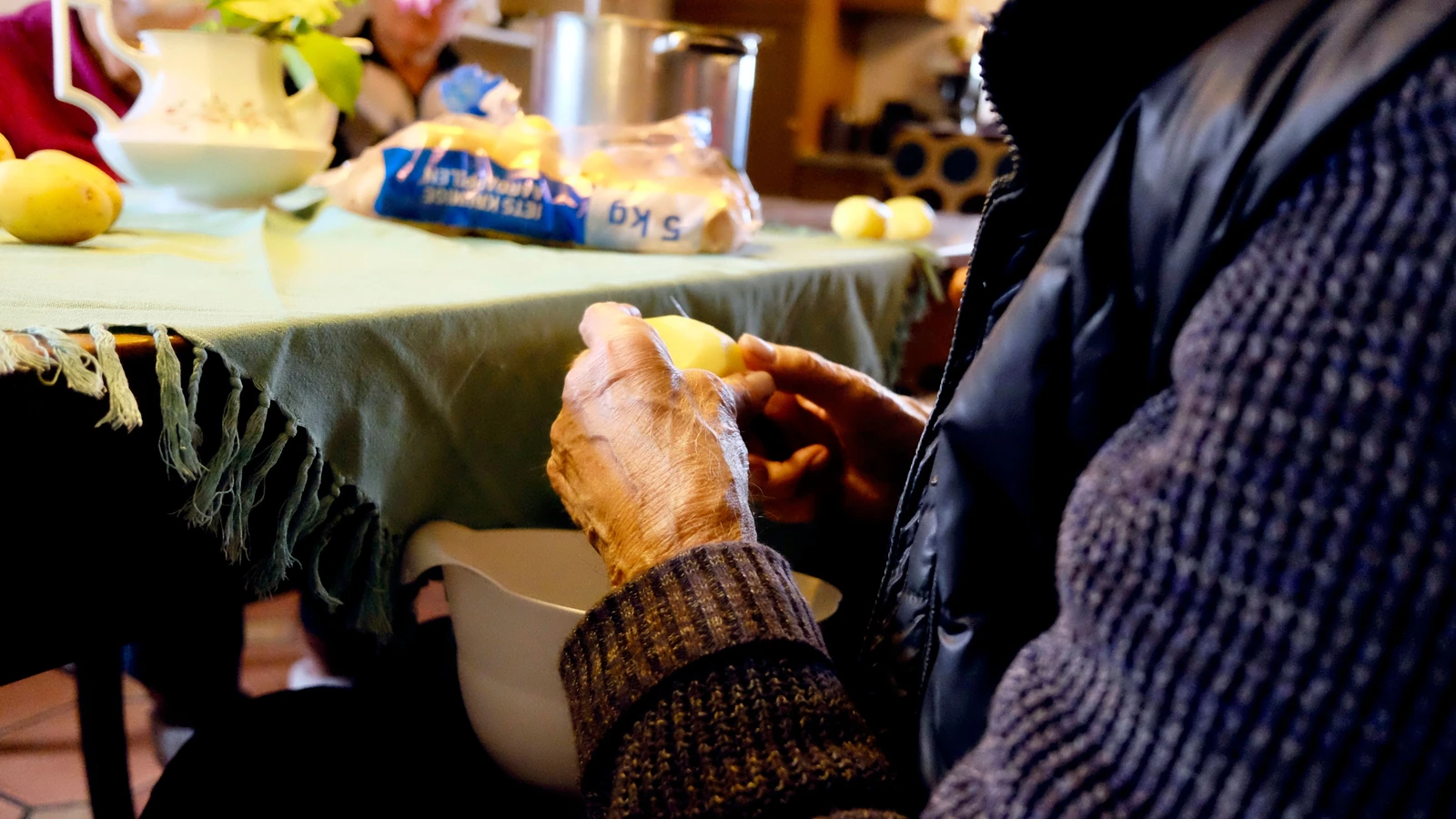 Un anziano sbuccia le patate a un tavolo della cucina, mostrando la routine culinaria.