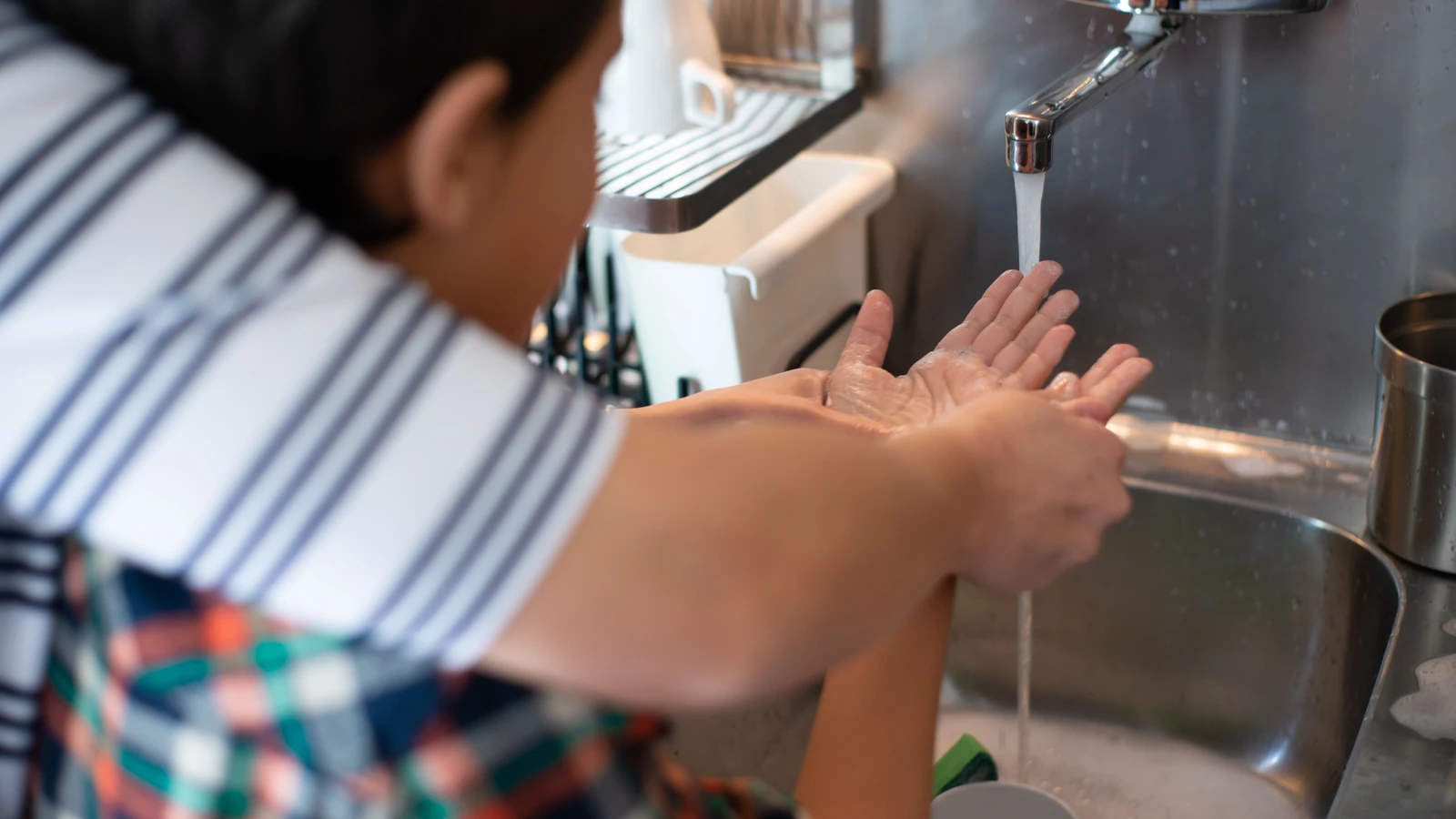 Un bambino che pratica l'igiene imparando a lavarsi le mani sotto la supervisione di un adulto al lavandino della cucina.