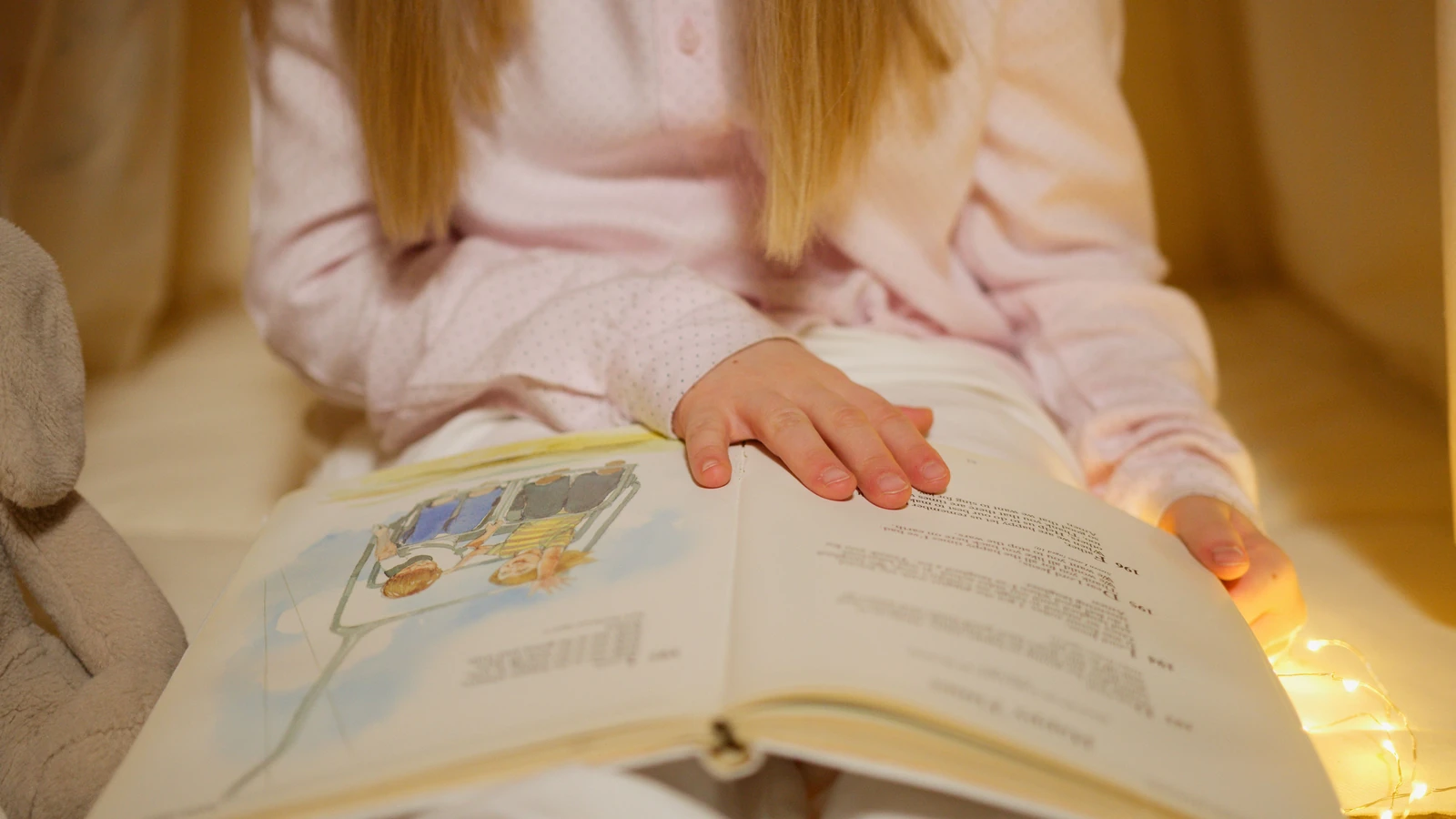 Una giovane ragazza in pigiama che legge un libro di storie in una calda e accogliente camera da letto.