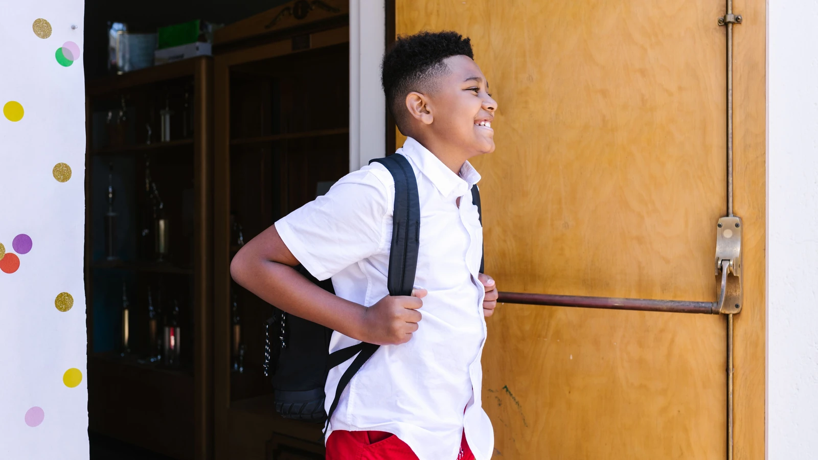 Un ragazzo sorridente con uno zaino entra a scuola, pronto per un nuovo anno accademico. — RDNE Stock project – Pexels
