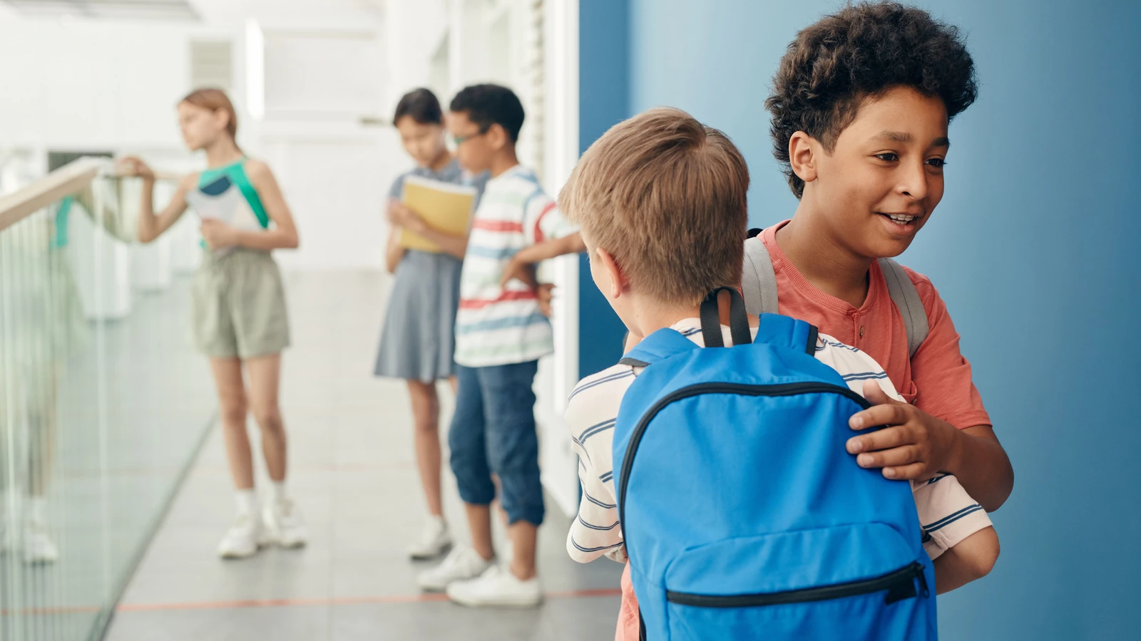 Gruppo di bambini che socializzano in un luminoso corridoio scolastico, indossando zaini.