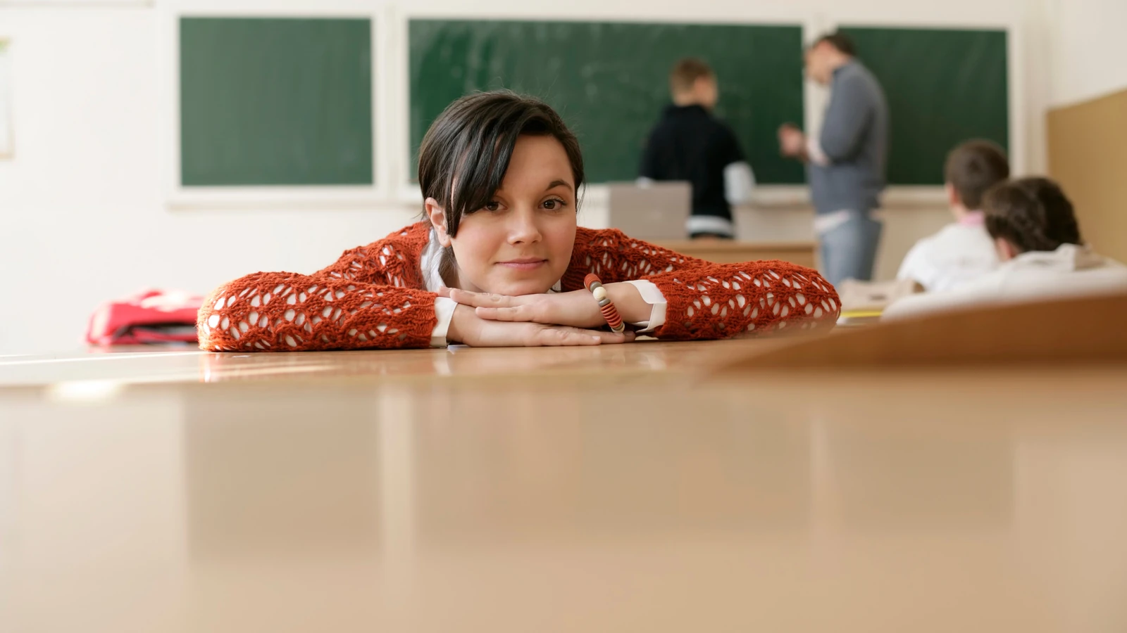 Una giovane studentessa appoggia la testa su un banco in aula, con un focus sull'istruzione e il relax. — BOOM 💥 Photography – Pexels
