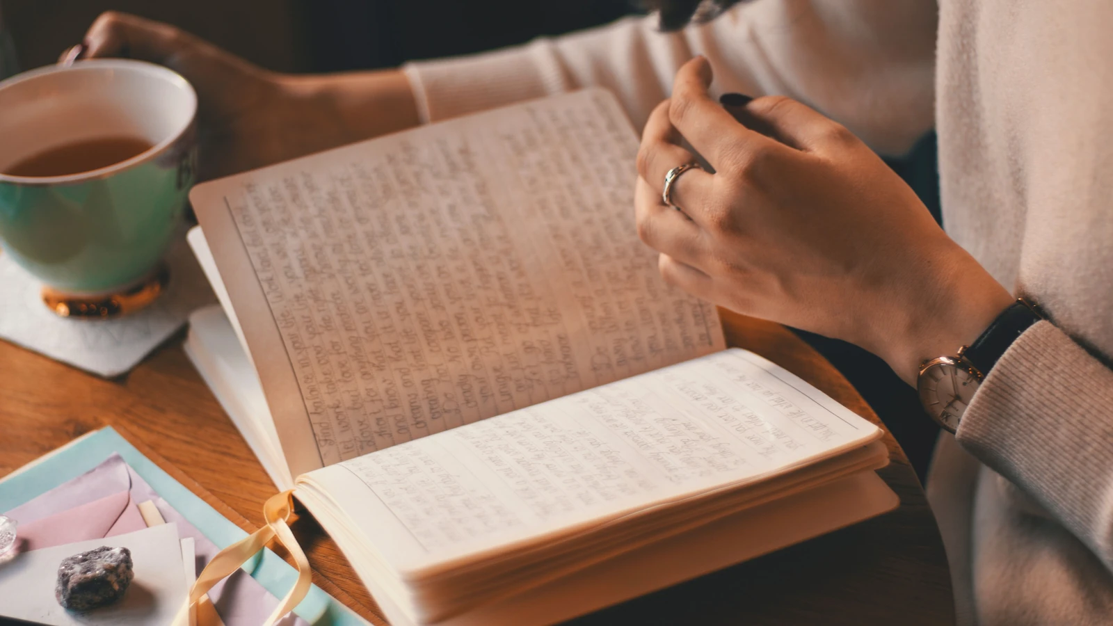 Una donna scrive in un diario mentre si gusta una tazza di caffè a un tavolo di legno.