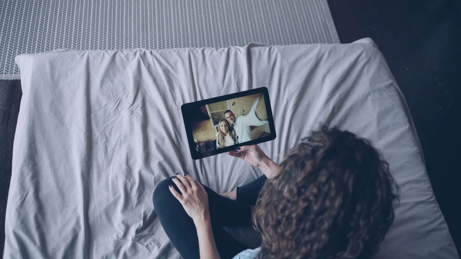 Vista dall'alto di una donna che utilizza un tablet per una videochiamata mentre è seduta su un letto.