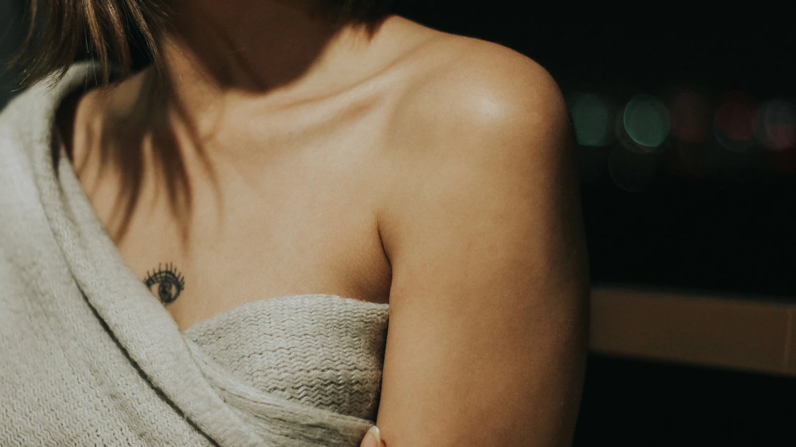 Primo piano intimo della spalla di una donna e del suo tatuaggio, avvolta in un tessuto accogliente.