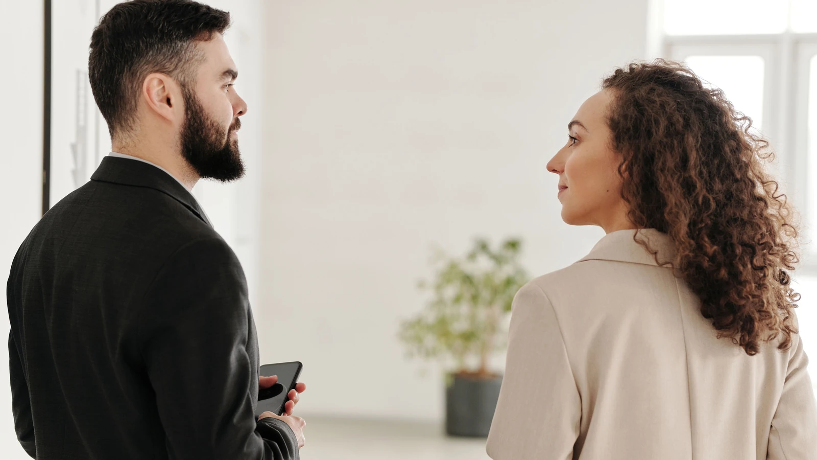 Un uomo e una donna in abbigliamento da lavoro conversano all'interno di un ufficio.