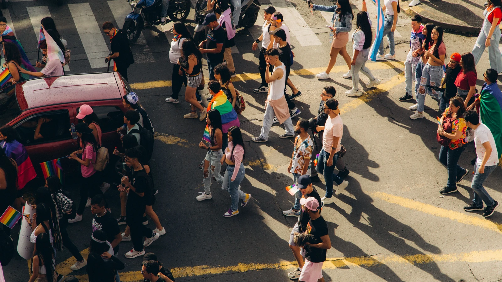 Una vivace parata del pride con partecipanti diversi e bandiere rainbow catturata dall'alto in una giornata di sole.
