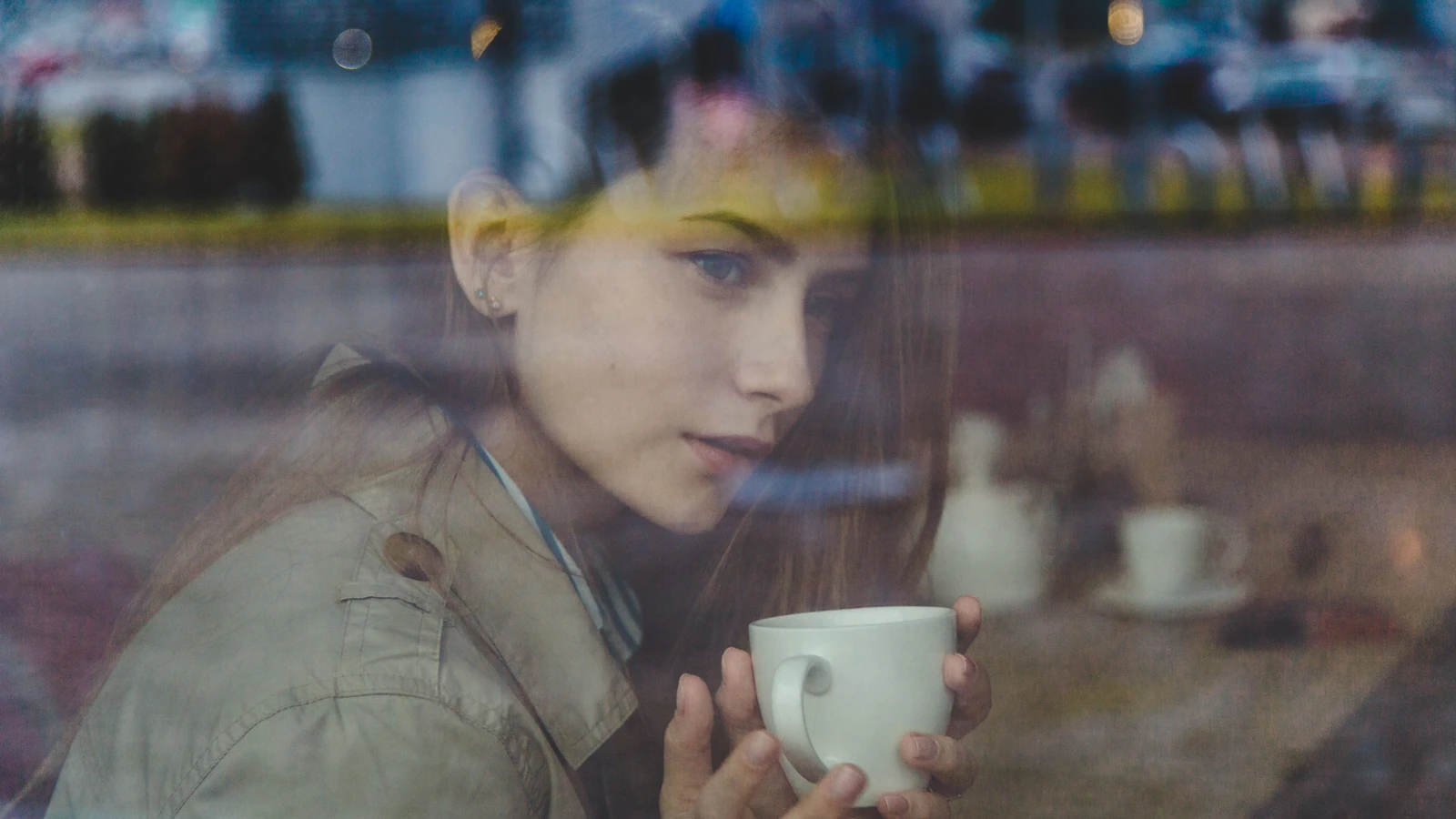 Donna caucasica con una tazza di ceramica che guarda attraverso una finestra di un caffè, pacifica e riflessiva.