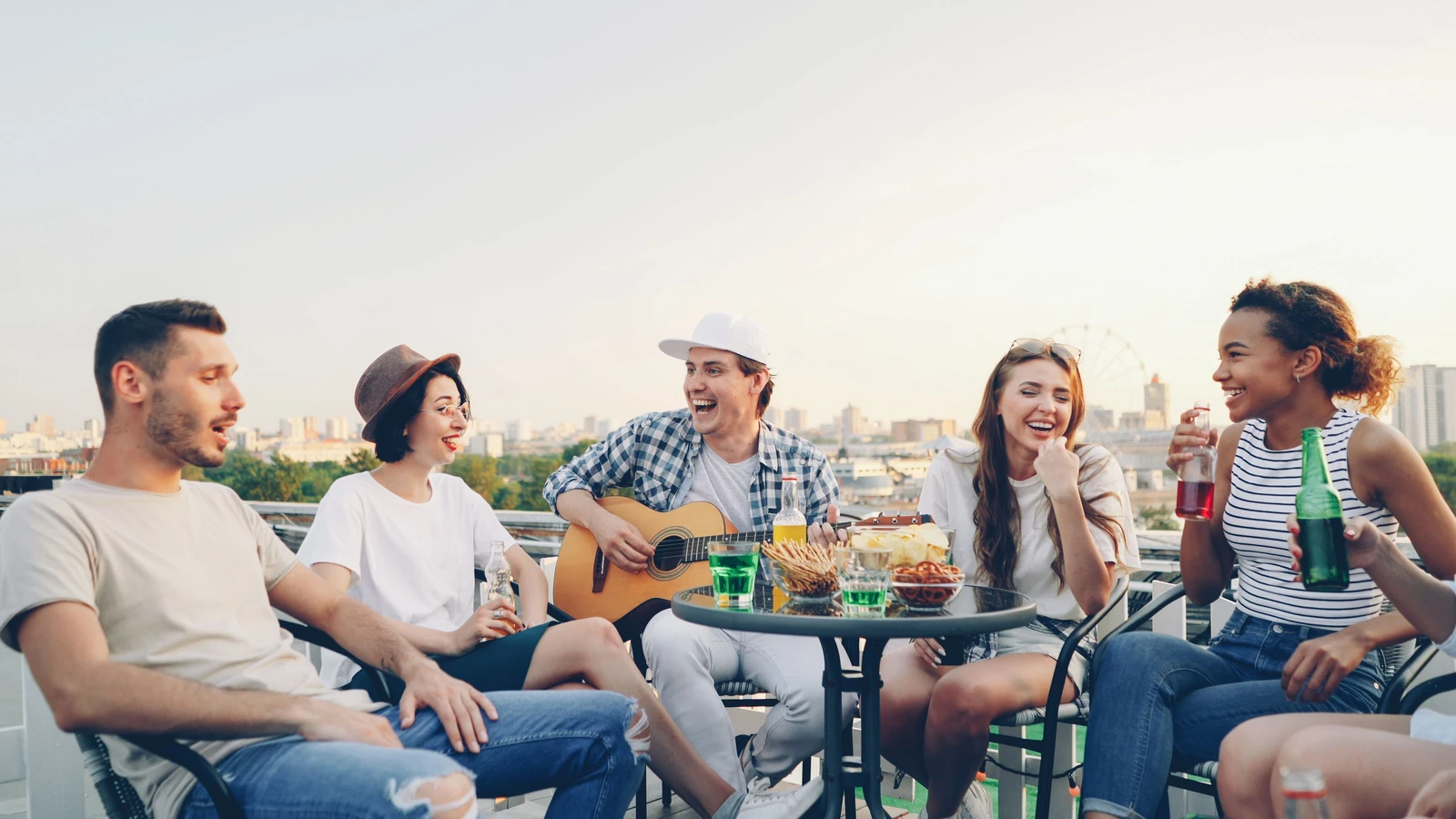 Un gruppo di amici si diverte su una terrazza con musica e bevande.