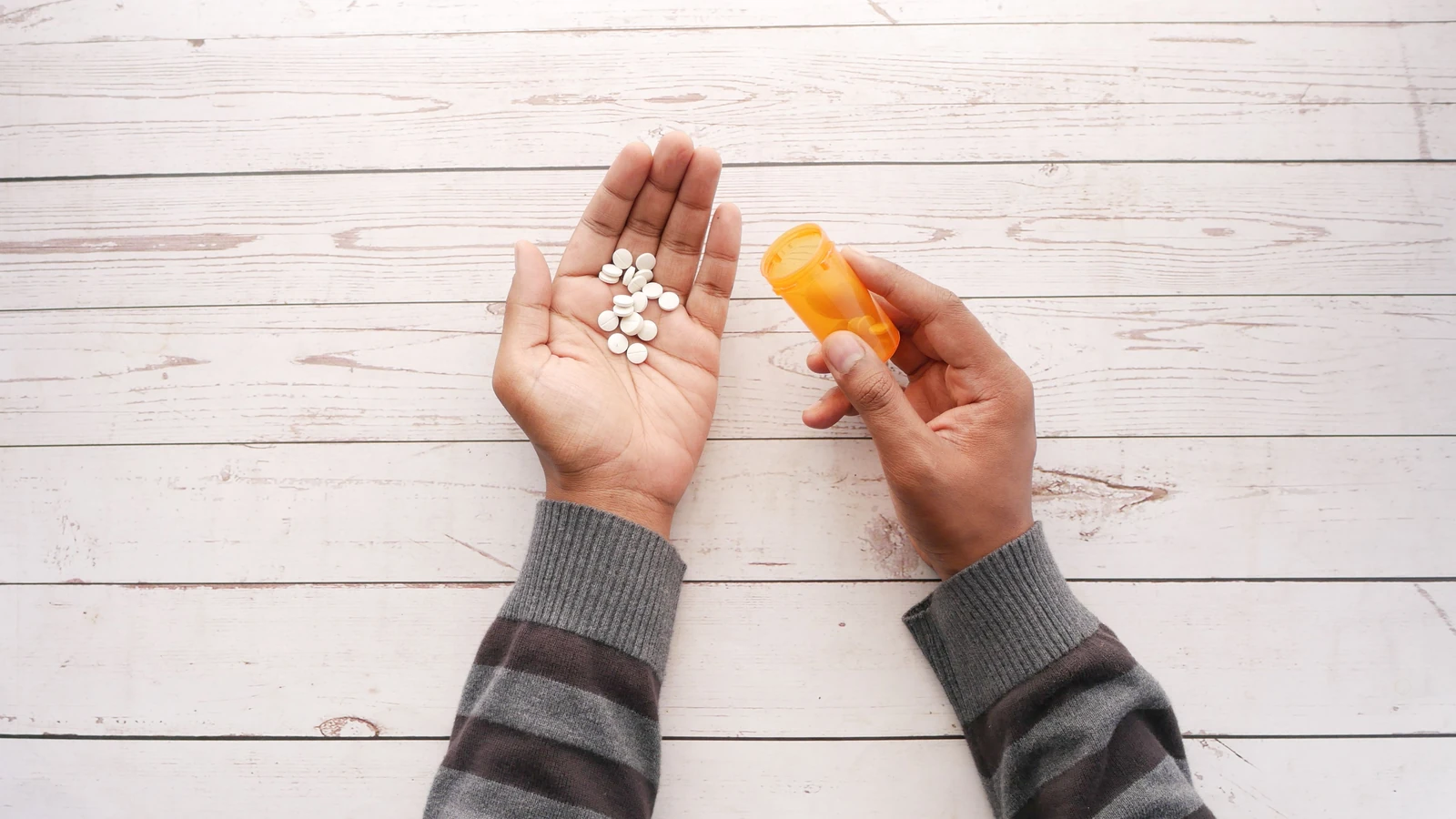 Primo piano di mani che tengono pillole di farmaco con una bottiglia di prescrizione su una superficie di legno.