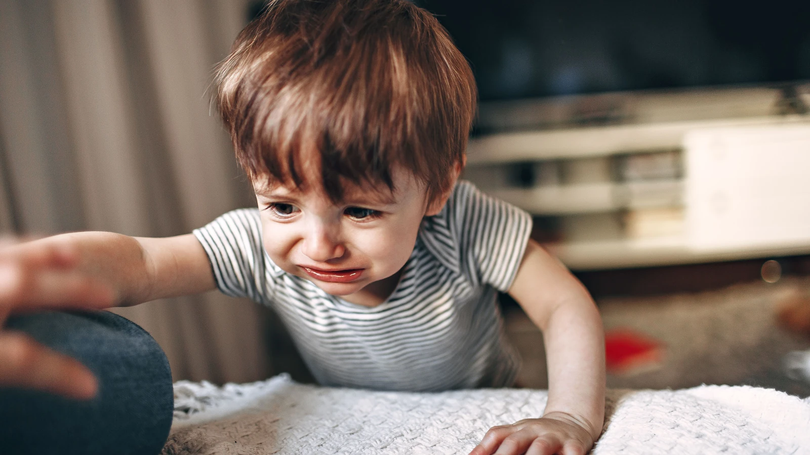 Un bambino piccolo con maglietta a righe allunga la mano piangendo