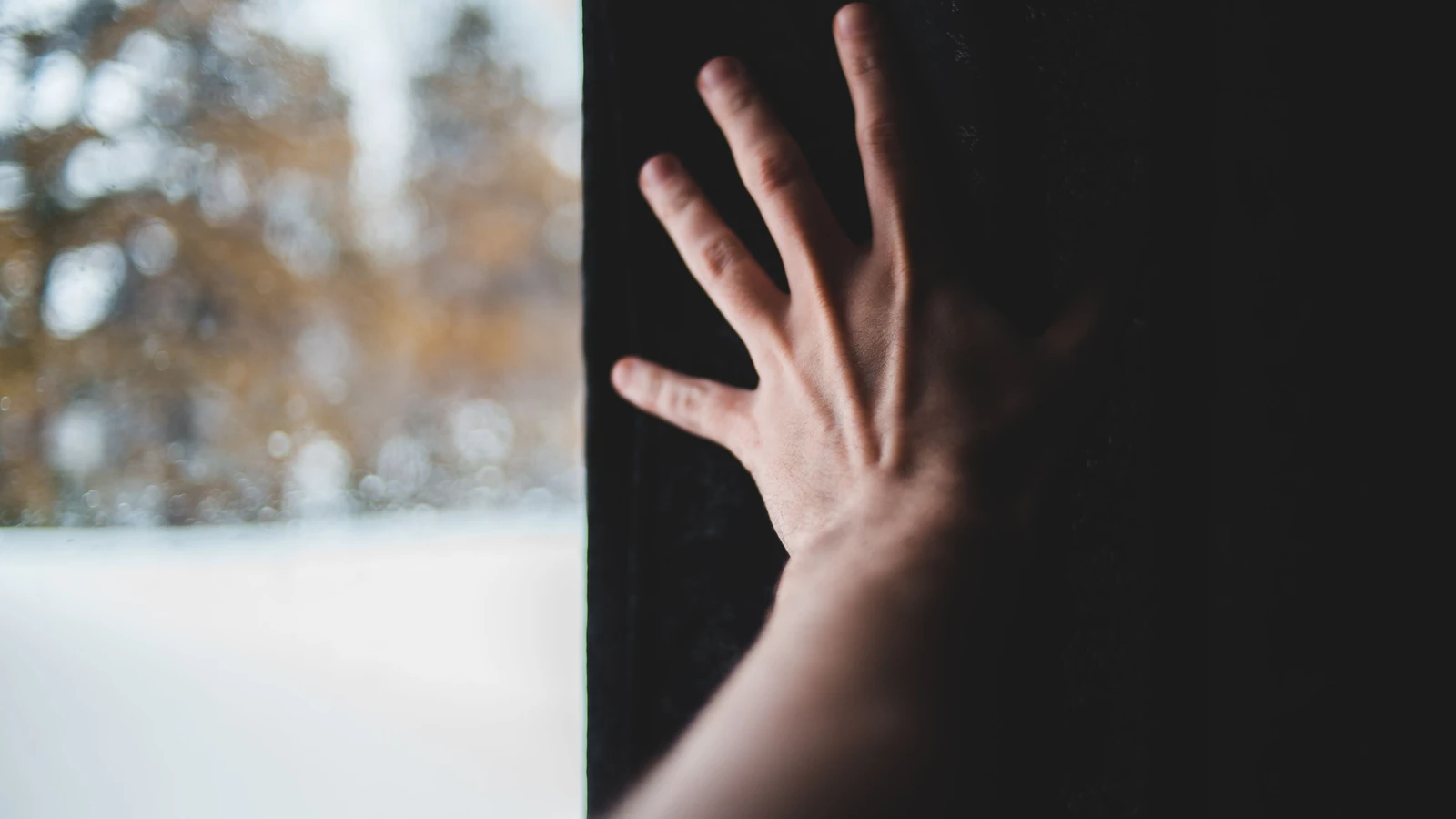Primo piano di una mano che tocca una finestra con la neve all'esterno, evocando solitudine e tranquillità.