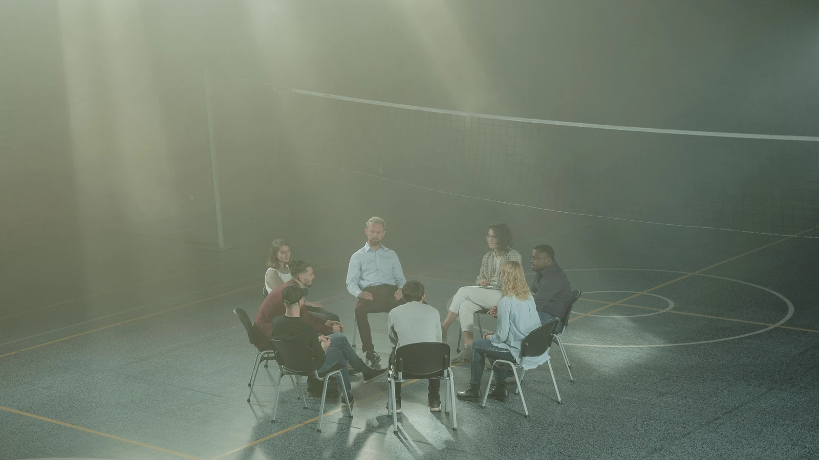 Un gruppo variegato si riunisce in una palestra per una sessione di terapia di supporto, con la luce del sole che filtrava attraverso la foschia.