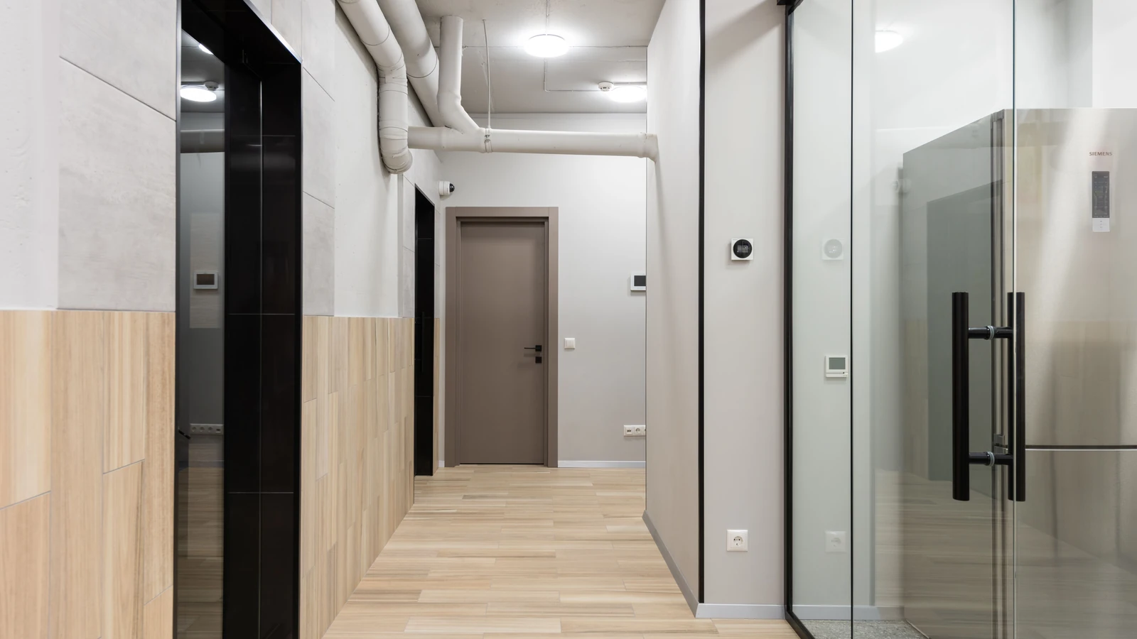 Un corridoio d'ufficio elegante e minimalista con pareti di vetro e pavimenti in legno.