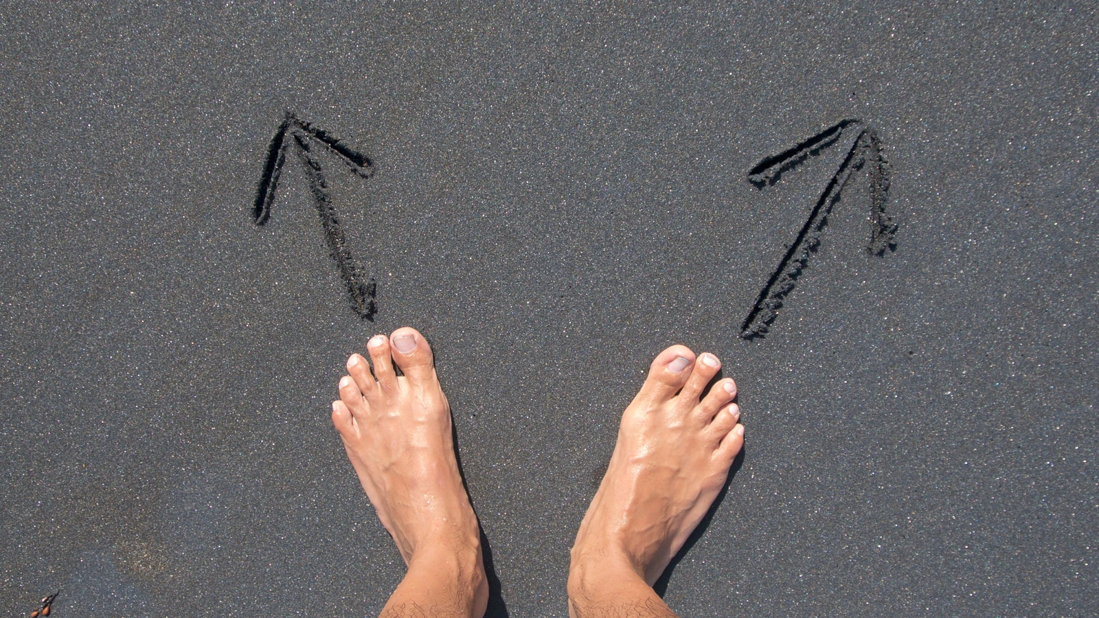 Un paio di piedi scalzi sulla sabbia della spiaggia di Bali con frecce disegnate, che simboleggiano scelta e direzione.