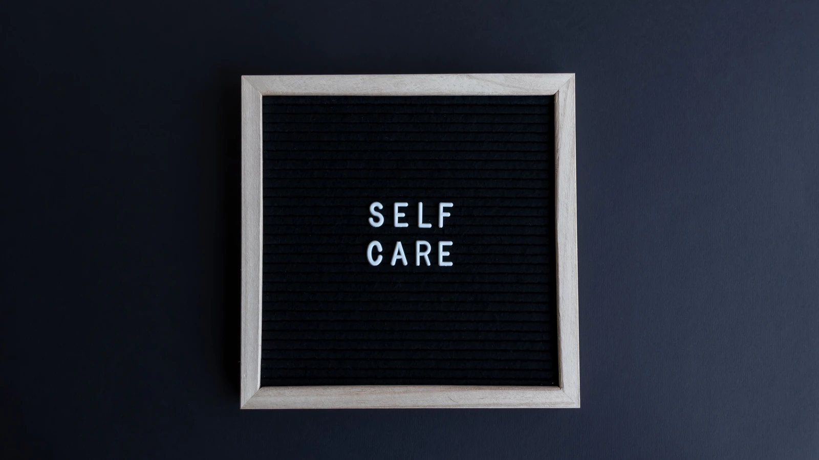 Un pannello di lettere minimalista che mostra 'CURA DI SE' su uno sfondo scuro, promuovendo la consapevolezza e il benessere.