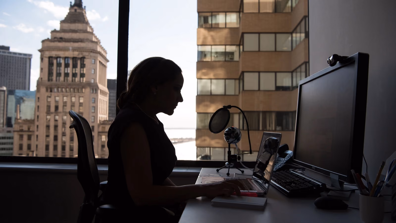 Silhouette di una donna che lavora a una scrivania in un ufficio urbano con vista sulla città. — Christina Morillo – Pexels