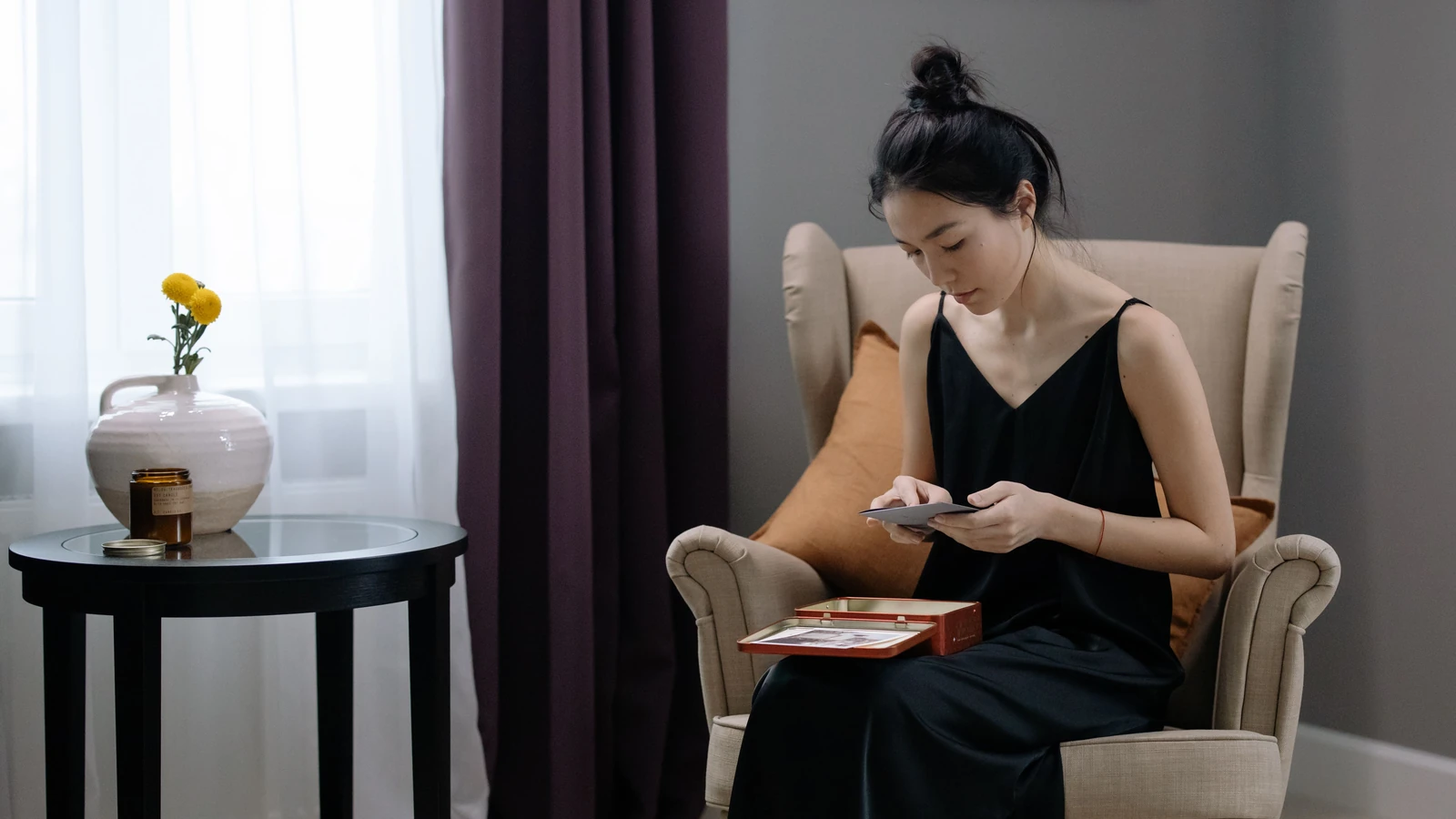Una donna in un abito nero è seduta su una poltrona beige, leggendo un libro in una stanza accogliente e soleggiata.