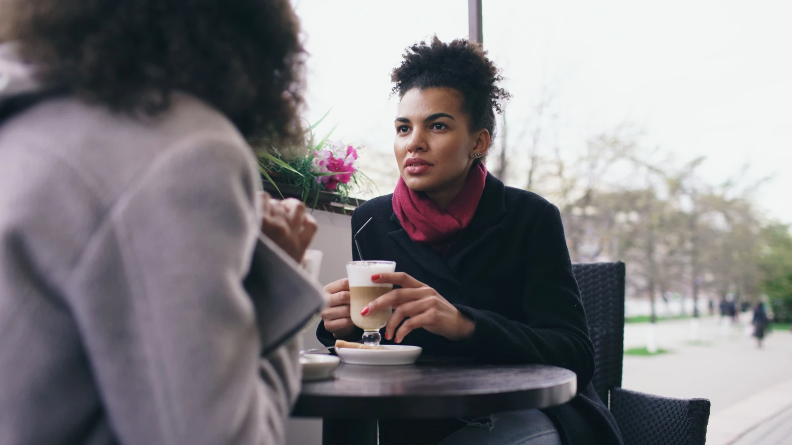 Due donne che conversano davanti a un caffè in un bar all'aperto in una giornata di sole.