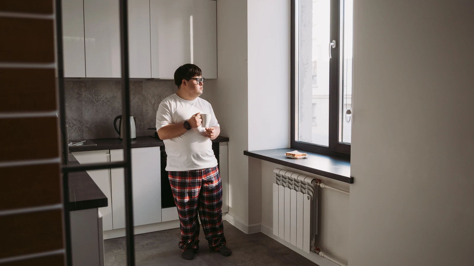 Giovane con sindrome di Down con una tazza in una cucina moderna, alla luce del giorno.
